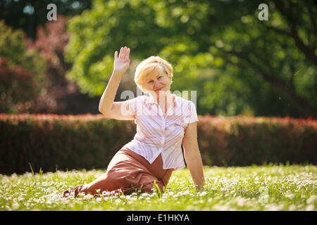 Maturity. European White Hair Woman sitting on Grass and having Fun Stock Photo