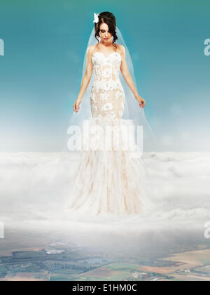 Bride in Wedding White Dress standing on a Cloud and Looking to the Ground Stock Photo