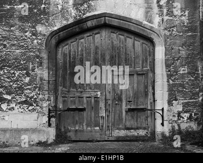 An old wooden double door set into a stone wall in black and white Stock Photo