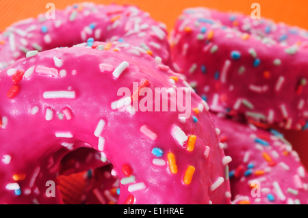 closeup of a pile of donuts coated with a pink frosting and sprinkles of different colors Stock Photo