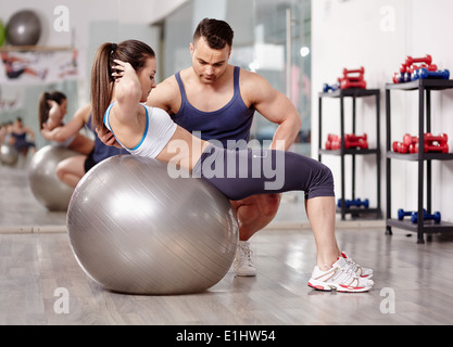 Personal trainer helping woman doing abs crunches with gym ball Stock Photo