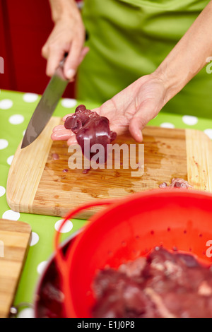 Woman's hands slicing liver for cooking, on a wooden board in the kitchen Stock Photo