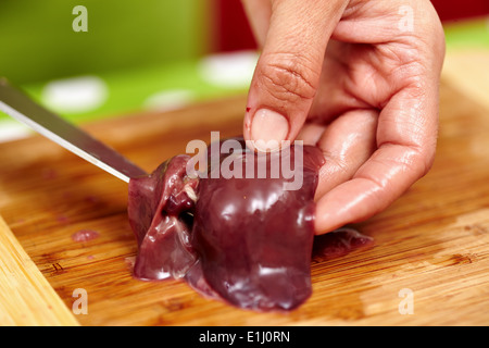 Woman's hands slicing liver for cooking, on a wooden board in the kitchen Stock Photo