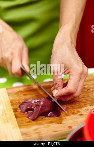 Woman's hands slicing liver for cooking, on a wooden board in the kitchen Stock Photo