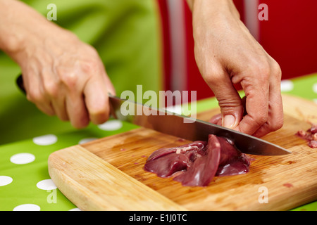 Woman's hands slicing liver for cooking, on a wooden board in the kitchen Stock Photo