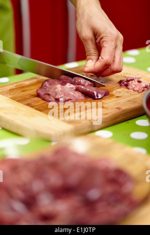 Woman's hands slicing liver for cooking, on a wooden board in the kitchen Stock Photo