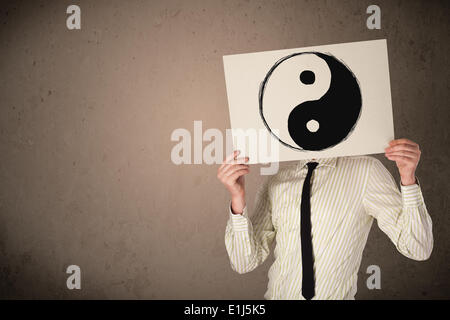 Businessman holding a paper with a yin-yang on it in front of his head Stock Photo