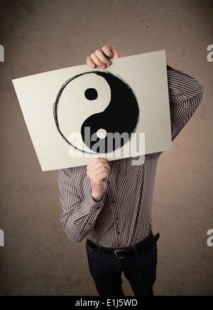 Businessman holding a paper with a yin-yang on it in front of his head Stock Photo