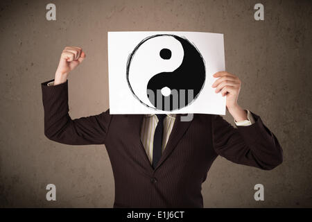 Businessman holding a paper with a yin-yang on it in front of his head Stock Photo