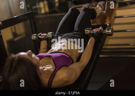 Mid adult woman using dumbbells on weight bench Stock Photo
