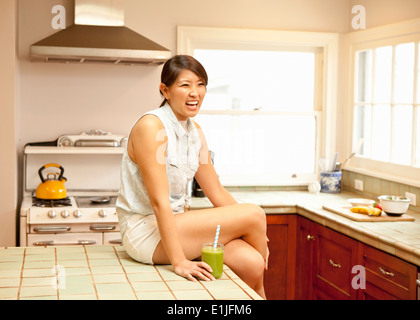 Young woman with green smoothie in kitchen Stock Photo