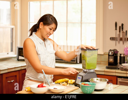 Young woman making green smoothie in kitchen