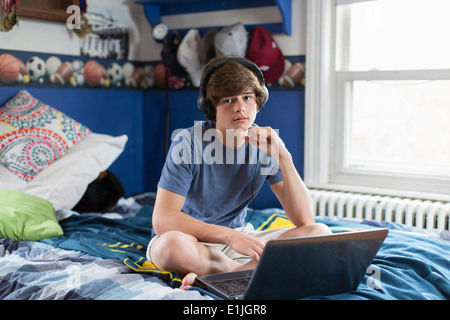 Teenage boy sitting on bed with laptop computer Stock Photo