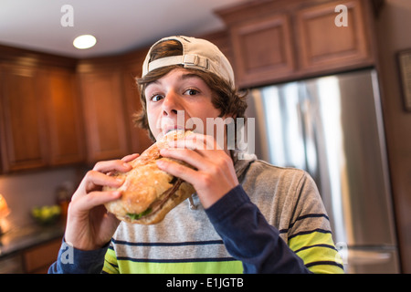 Teenage boy in kitchen biting large sandwich Stock Photo