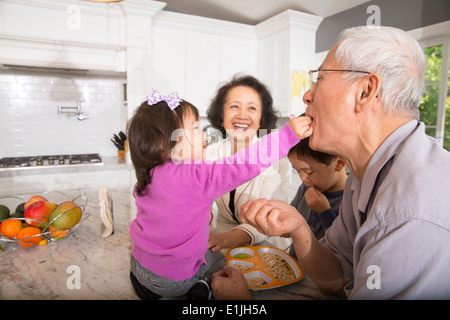 Female toddler feeding snack to grandfather in kitchen Stock Photo