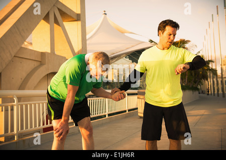 Exhausted male runner with trainer checking pulse Stock Photo