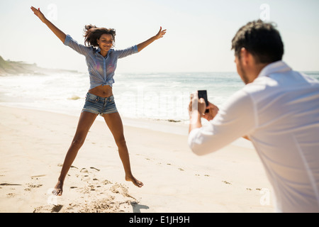 Mid adult man photographing girlfriend jumping, Arpoador beach, Rio De Janeiro, Brazil Stock Photo