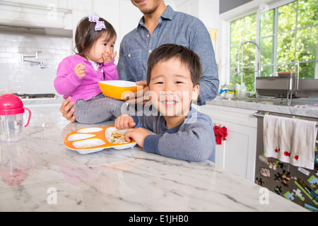 Mid adult man with two young children snacking in kitchen Stock Photo