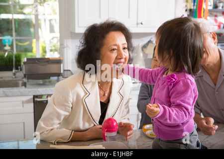 Female toddler feeding snack to grandmother in kitchen Stock Photo