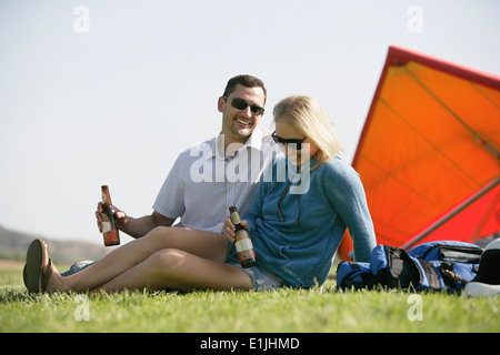 Couple relaxing with beer, hang glider in background Stock Photo