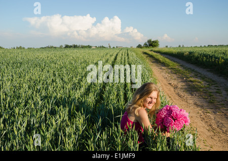 long village sand path and woman sitting with peony flower near rye field Stock Photo