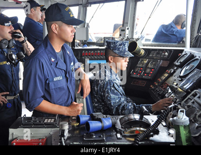 U.S. Navy Boatswain's Mate 3rd Class Jerome Arriola, center, and another Sailor, right, man the helm of the guided missile frig Stock Photo