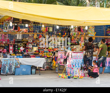 Sidewalk Toy Shop. Two men and a young girl shop at a very well stocked street vendor's toy stall in the market in Tulum. Stock Photo