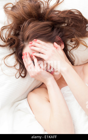 MODEL RELEASED Woman lying down with hands covering face smiling. Stock Photo