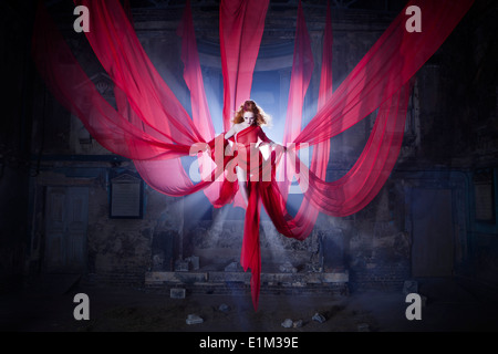 Dramatic SIren woman suspended by red fabric in old Gothic church location Stock Photo