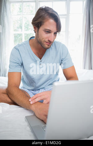Handsome smiling man sitting on bed using laptop Stock Photo