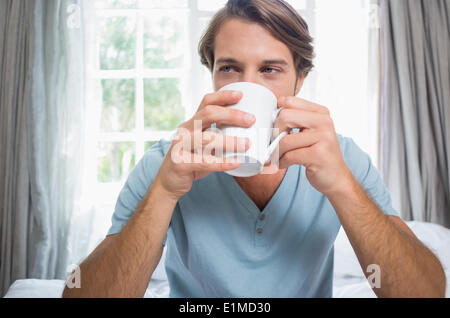 Handsome man sitting on bed drinking coffee Stock Photo