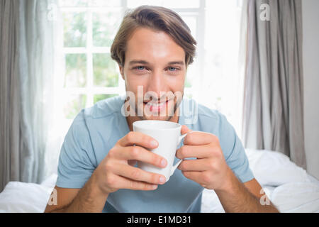 Handsome man sitting on bed drinking coffee Stock Photo