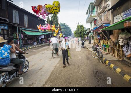 June 6, 2014 - Pantanaw, Ayeyarwady Region, Myanmar - An inflatable toy vendor walks down the street in Pantanaw, a town in the Irrawaddy Delta (or Ayeyarwady Delta) in Myanmar. The region is Myanmar's largest rice producer, so its infrastructure of road transportation has been greatly developed during the 1990s and 2000s. Two thirds of the total arable land is under rice cultivation with a yield of about 2,000-2,500 kg per hectare. FIshing and aquaculture are also important economically. Because of the number of rivers and canals that crisscross the Delta, steamship service is widely availabl Stock Photo