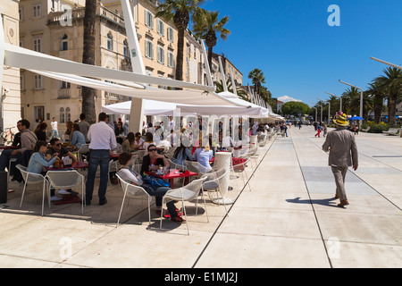Local people and tourists walk along the Riva in split croatia. Cafes and restaurants line the side. Stock Photo