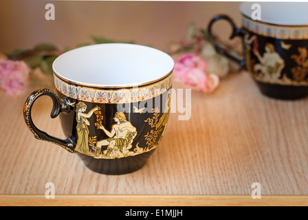 The beautiful tea cups decorated with a list with gold with the image of scenes from antique life. Stock Photo