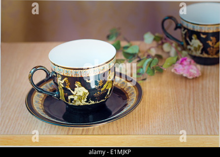 The beautiful tea cups decorated with a list with gold with the image of scenes from antique life. Stock Photo
