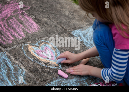 Girl drawing a chalk heart on a concrete sidewalk. Stock Photo