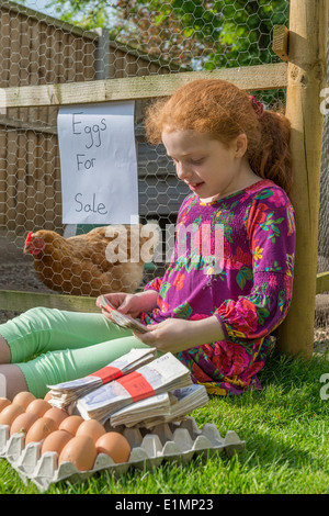 Little girl entrepreneur sits with thousands of pounds whilst selling hens eggs. Stock Photo