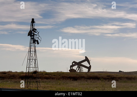 Watford City, North Dakota - Oil is pumped near an old farm windmill in the Bakken shale formation. Stock Photo