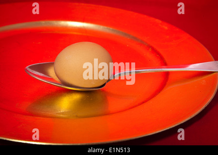 Egg and spoon.  Hen's egg on silver spoon on a red plate Stock Photo