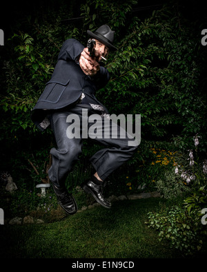 A man dressed in a vintage style suit and aiming a gun while jumping in mid-air. Stock Photo