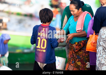 Boy in shirt with number “10” and inscriptions: “Messi” and “unicef” in scenery of Tanjung Luar (Lombok) during fish market Stock Photo