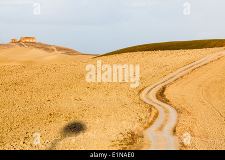 Landscape with buildings on the hill, winding field road and ploughed land in region of Mucigliani (between Siena and Asciano), Tuscany Stock Photo