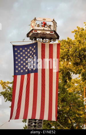 Garden City, New York, USA. 6th June, 2014. A large American Flag was suspended from a cherry picker high over the intersection of Franklin Avenue and 7th Street, during the 17th Annual Garden City Belmont Stakes Festival, celebrating the 146th running of Belmont Stakes at nearby Elmont the next day. There was street festival family fun with live bands, food, pony rides and more, and a main sponsor of this Long Island night event was The New York Racing Association Inc. © Ann Parry/ZUMAPRESS.com/Alamy Live News Stock Photo