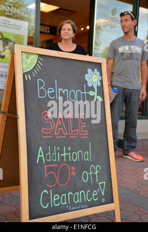 Garden City, New York, U.S. - June 6, 2014 -  ANTHONY RANDOLPHI of Valley Stream, on staff at New York Running Co, is by a chalkboard easel sign announcing the store's Belmont Sale, during the 17th Annual Garden City Belmont Stakes Festival, celebrating the 146th running of Belmont Stakes at nearby Elmont the next day. There was street festival family fun with live bands, food, pony rides and more, and a main sponsor of this Long Island night event was The New York Racing Association Inc. Stock Photo
