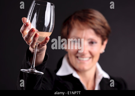 pretty old woman rising up a glass of wine with glaze on camera with focus on the glass Stock Photo