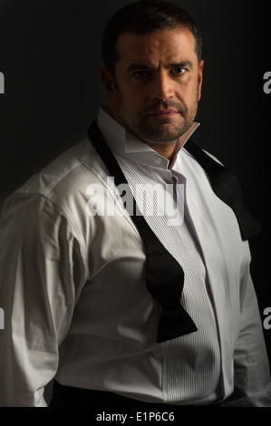 Low key portrait of handsome male wearing shirt and bow tie looking into the camera. This is shot with a dark background. Stock Photo
