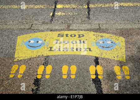 Stop Look Listen sign with smiley faces and footprints painted on a roadside kerb near a primary school road crossing. Scotland UK Britain Stock Photo