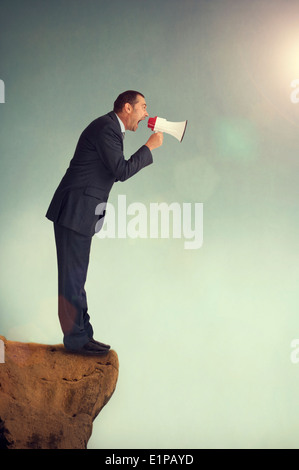 businessman with loudhailer on the edge of a cliff shouting Stock Photo