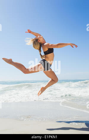 Fit blonde jumping gracefully on the beach Stock Photo